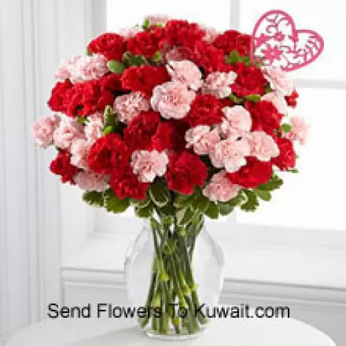 36 Oeillets (18 rouges et 18 roses) avec des remplissages saisonniers et un bâton de cœur de la Saint-Valentin dans un vase en verre